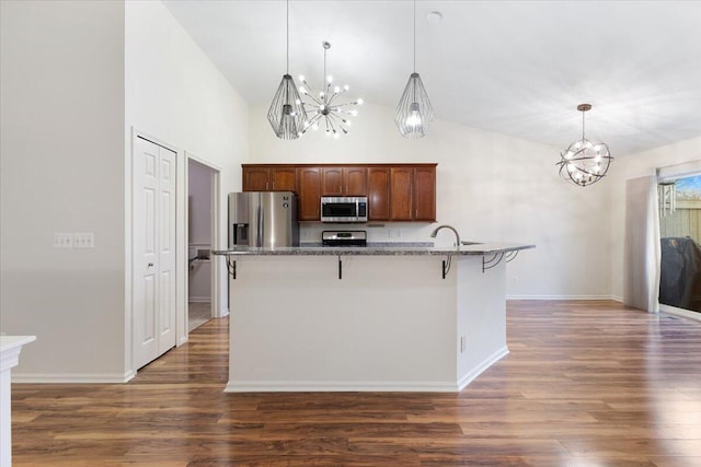 kitchen with wood finished floors, dark stone counters, appliances with stainless steel finishes, a kitchen breakfast bar, and a notable chandelier