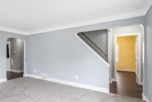 carpeted empty room featuring arched walkways, ornamental molding, visible vents, stairway, and baseboards