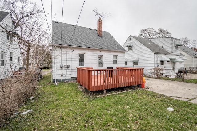 back of property featuring a yard, a shingled roof, a deck, and a chimney