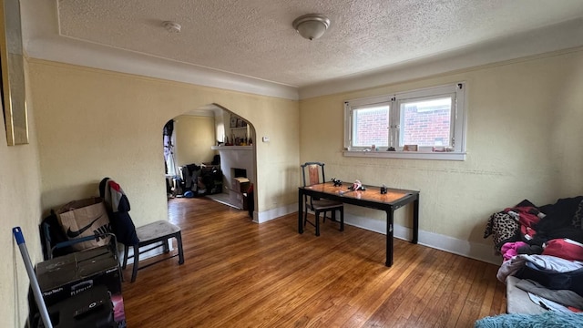 office area featuring a textured ceiling, arched walkways, wood-type flooring, baseboards, and a textured wall