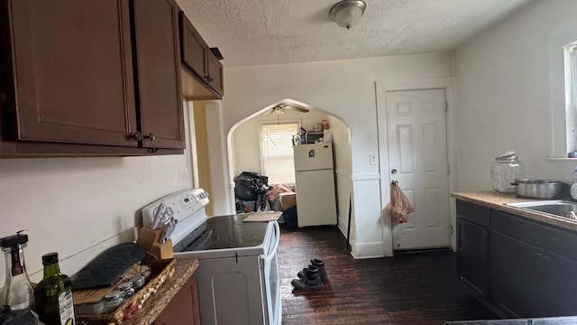 kitchen with white appliances, arched walkways, dark wood-style flooring, a sink, and a textured ceiling