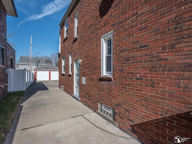 view of side of home featuring driveway, fence, brick siding, a garage, and an outdoor structure