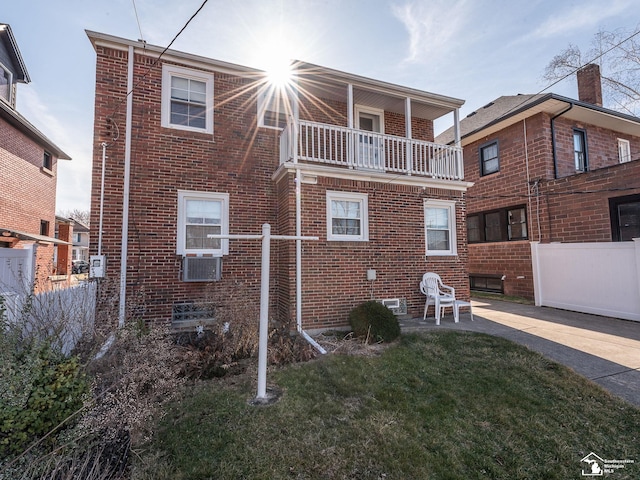 rear view of house with fence, a balcony, brick siding, and a yard