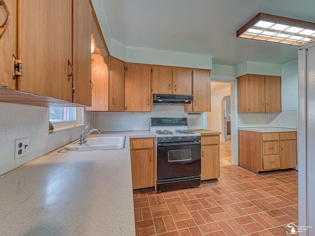 kitchen with a sink, range with gas stovetop, light countertops, under cabinet range hood, and brick patterned floor
