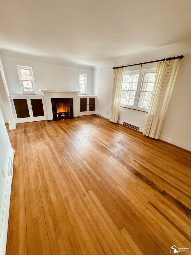 unfurnished living room with a tile fireplace, visible vents, and light wood-style floors