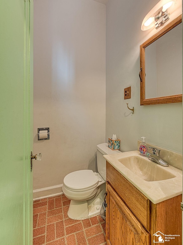 half bathroom with baseboards, vanity, and toilet