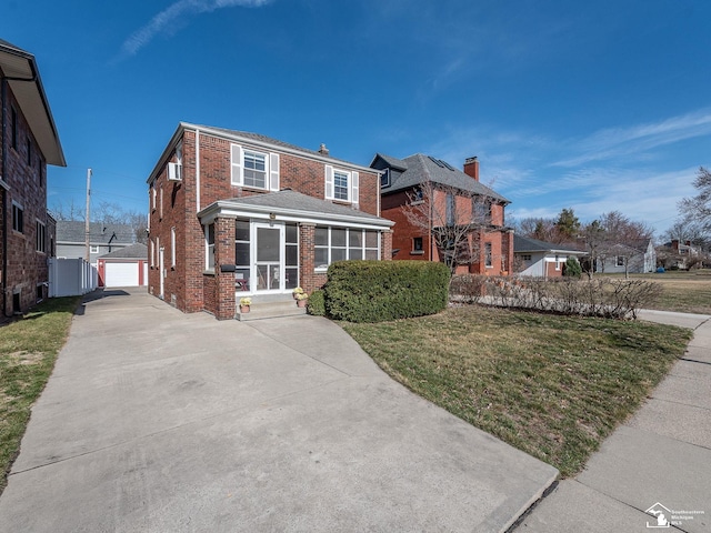 view of front of house featuring a detached garage, an outdoor structure, a front yard, brick siding, and a sunroom