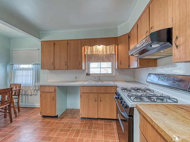 kitchen featuring brick patterned floor, under cabinet range hood, light countertops, a sink, and gas stove