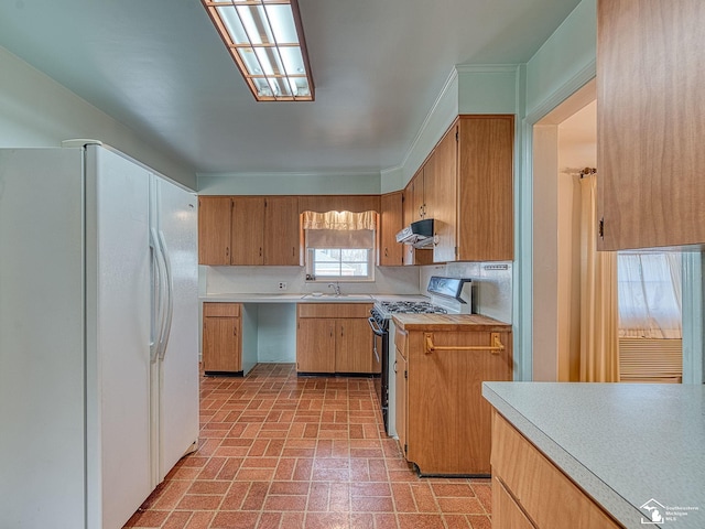 kitchen with freestanding refrigerator, range with gas stovetop, light countertops, under cabinet range hood, and brick patterned floor
