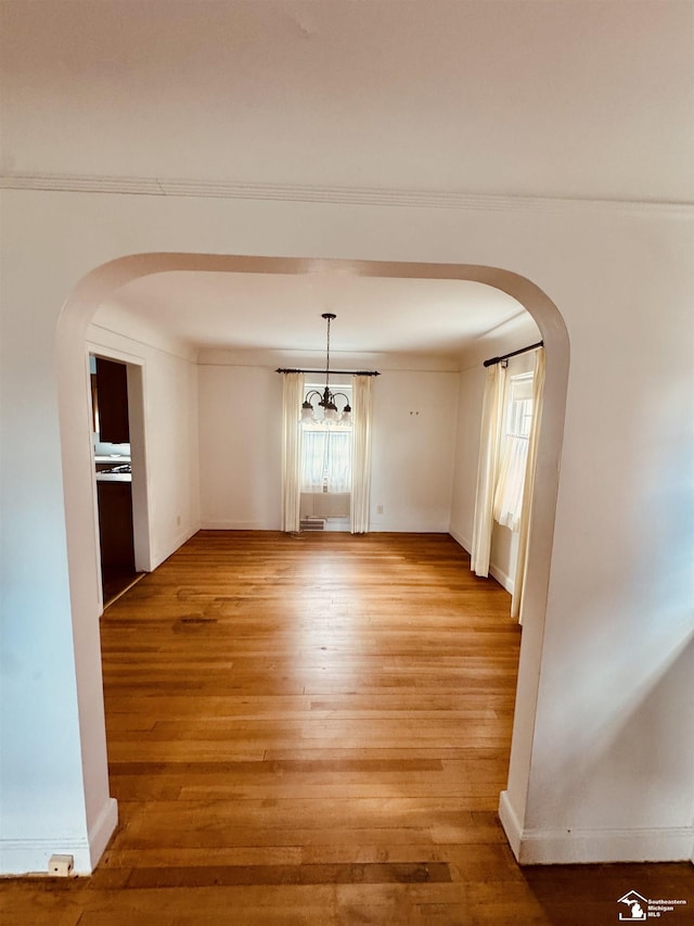 unfurnished dining area with baseboards, arched walkways, a notable chandelier, and light wood-style flooring