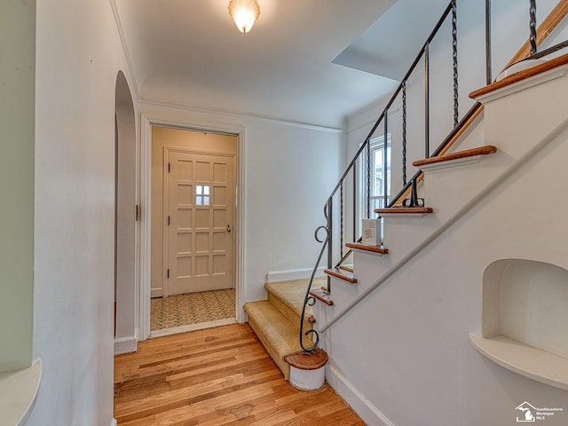 entryway with stairway, crown molding, arched walkways, light wood finished floors, and baseboards