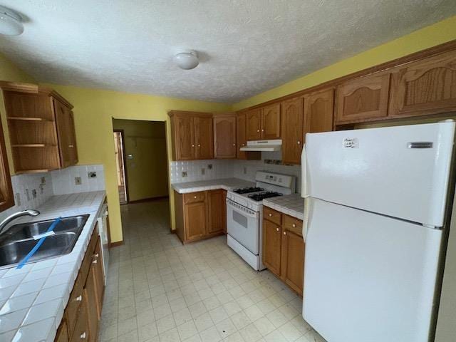 kitchen with a sink, open shelves, tile countertops, under cabinet range hood, and white appliances