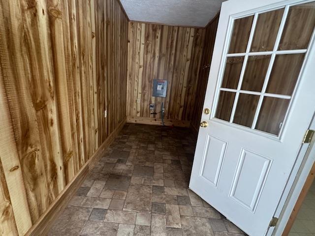 corridor with a textured ceiling, wood walls, and stone finish floor