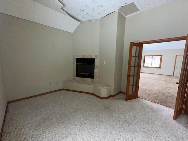 unfurnished living room featuring baseboards, high vaulted ceiling, a tile fireplace, and carpet