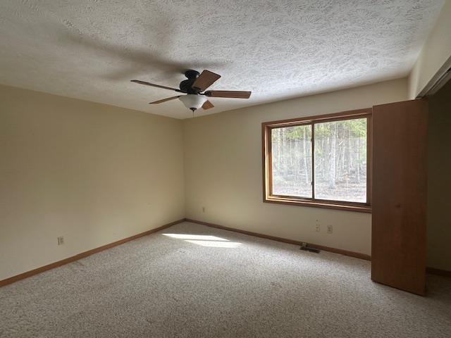unfurnished room featuring a ceiling fan, carpet floors, baseboards, and a textured ceiling