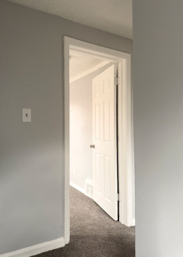hallway featuring carpet flooring, visible vents, baseboards, and a textured ceiling