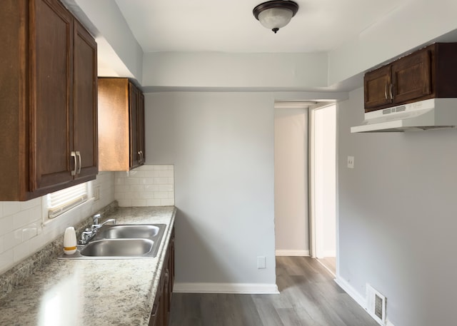 kitchen featuring light countertops, under cabinet range hood, backsplash, a sink, and visible vents