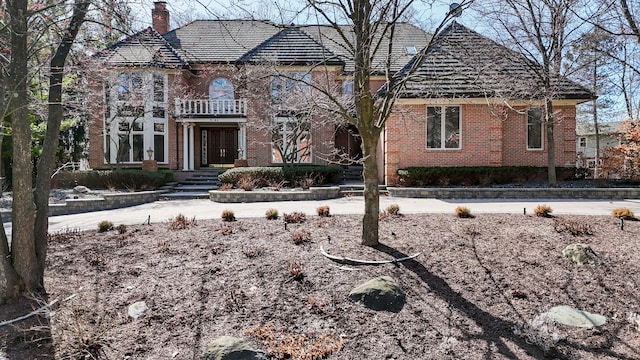 french provincial home featuring a chimney, brick siding, and a balcony