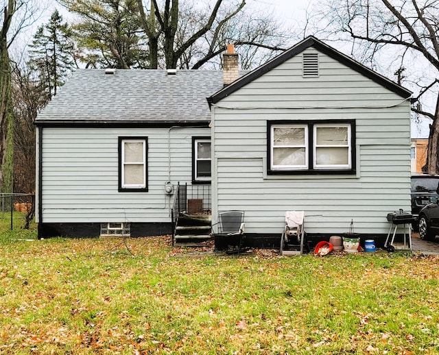 back of property with a shingled roof, a lawn, fence, and a chimney