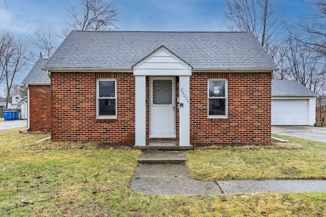 bungalow-style house with a front lawn, an outbuilding, brick siding, and roof with shingles