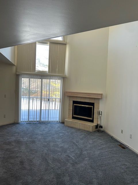 26766 Plumgrove Ln Unit 56, Farmington Hills, MI 48334 - unfurnished living room with a towering ceiling, baseboards, a tiled fireplace, and carpet floors