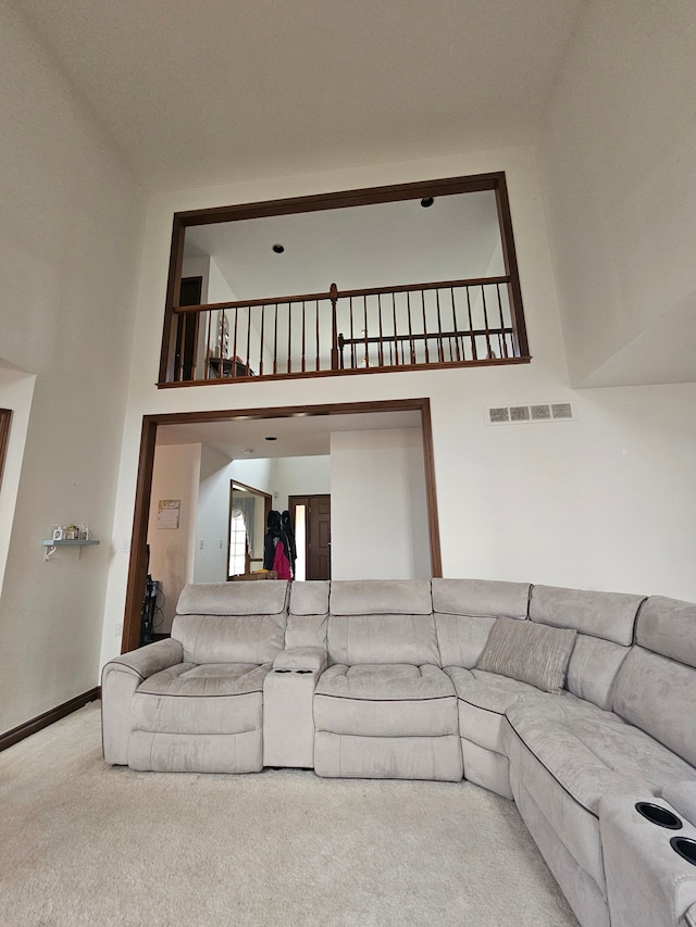 living area with visible vents, baseboards, carpet flooring, and a high ceiling