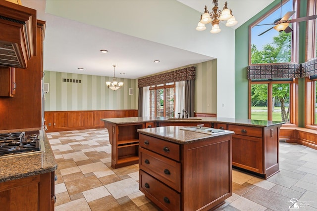 8650 Stone Rd, Maybee, MI 48159 - kitchen featuring a chandelier, an island with sink, a wainscoted wall, brown cabinets, and dark stone countertops