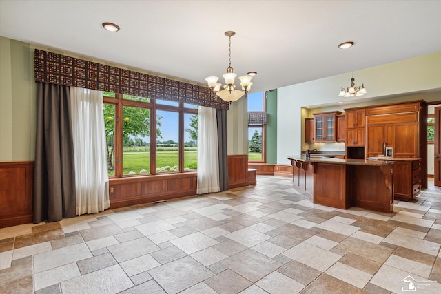 8650 Stone Rd, Maybee, MI 48159 - kitchen with a chandelier, stone tile floors, brown cabinetry, glass insert cabinets, and wainscoting