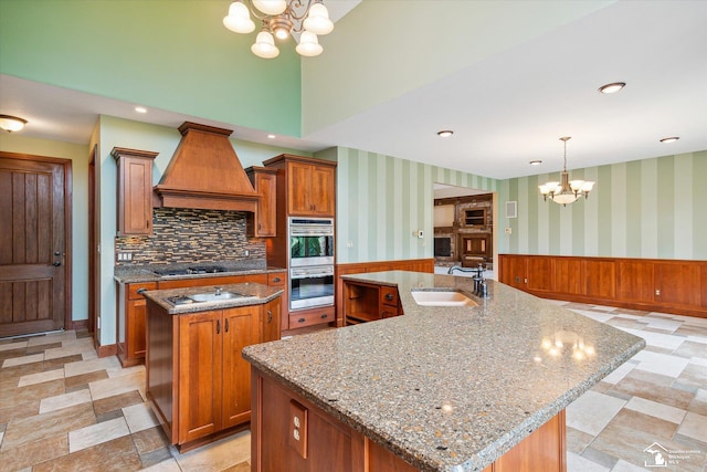 8650 Stone Rd, Maybee, MI 48159 - kitchen with a chandelier, an island with sink, premium range hood, double oven, and brown cabinetry