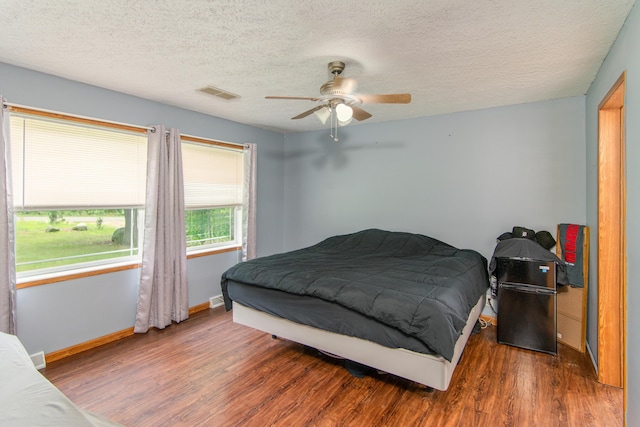 bedroom featuring a textured ceiling, wood finished floors, visible vents, and baseboards