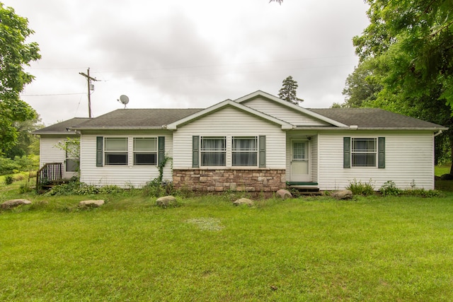 rear view of house with stone siding, a yard, and roof with shingles