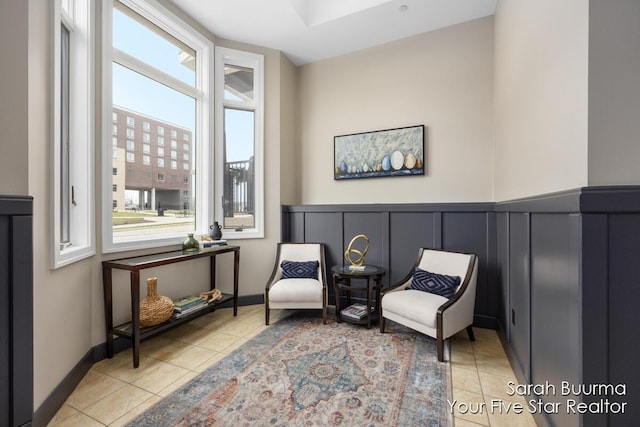 sitting room with baseboards, a decorative wall, and light tile patterned floors