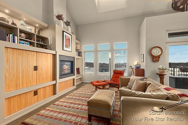living area featuring built in features, a towering ceiling, a glass covered fireplace, and plenty of natural light