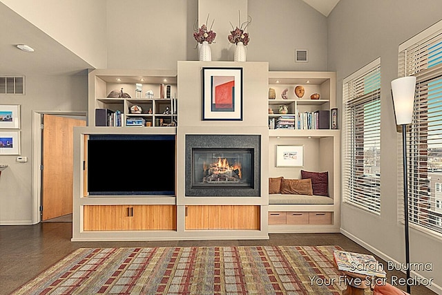 unfurnished living room with built in shelves, a high ceiling, a glass covered fireplace, baseboards, and visible vents