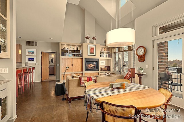 dining area with visible vents, a high ceiling, a lit fireplace, and built in features