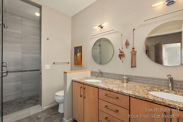 bathroom with a stall shower, double vanity, toilet, and a sink