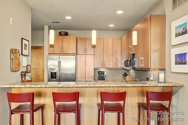 kitchen with a peninsula, appliances with stainless steel finishes, light stone countertops, and decorative backsplash