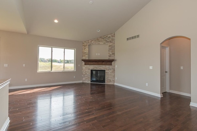 unfurnished living room with baseboards, visible vents, arched walkways, a stone fireplace, and dark wood-type flooring