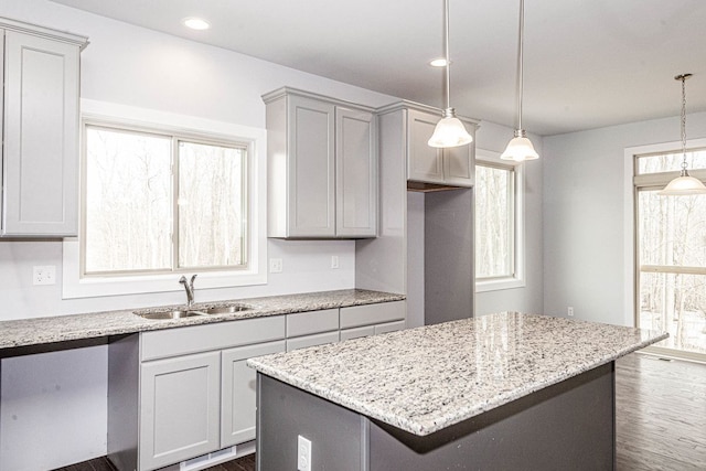 kitchen with a sink, light stone countertops, a kitchen island, and pendant lighting