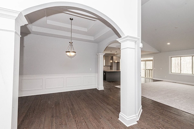 unfurnished dining area with decorative columns, arched walkways, a raised ceiling, and dark wood-style flooring