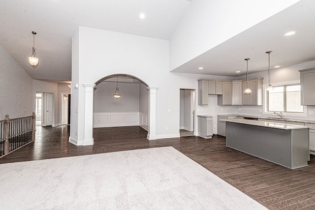 kitchen featuring dark wood-style floors, ornate columns, a kitchen island, arched walkways, and gray cabinetry