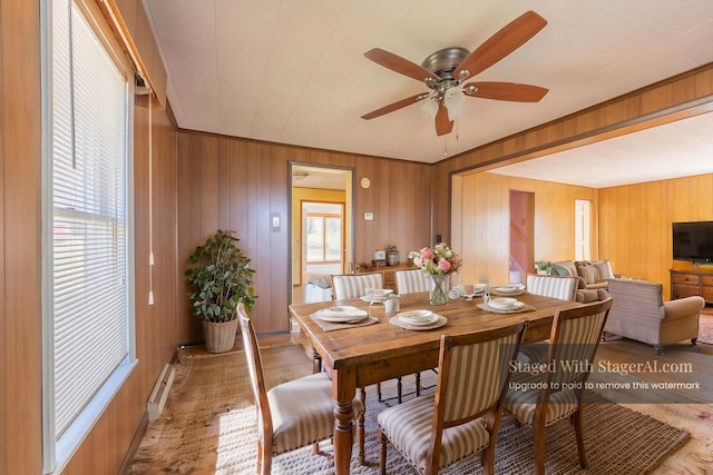 dining area featuring baseboard heating, a ceiling fan, and wood walls