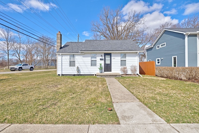 bungalow with a chimney, a shingled roof, fence, and a front lawn
