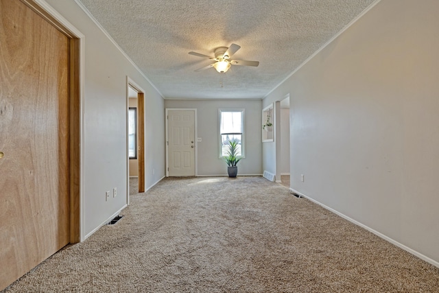 carpeted empty room featuring crown molding, baseboards, a textured ceiling, ceiling fan, and visible vents