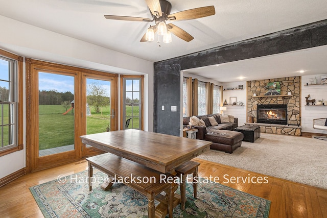 dining area with baseboards, ceiling fan, a fireplace, and light wood-style flooring