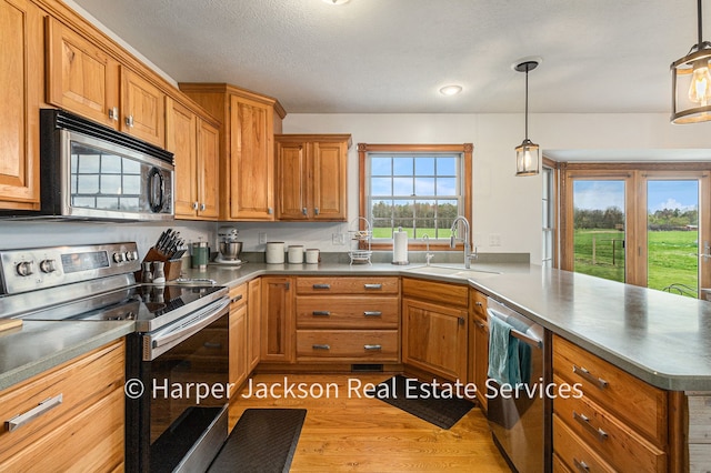 kitchen featuring wood finished floors, appliances with stainless steel finishes, brown cabinets, a sink, and a peninsula