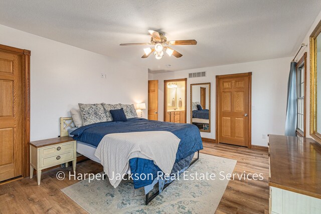 bedroom with connected bathroom, visible vents, baseboards, wood finished floors, and a ceiling fan