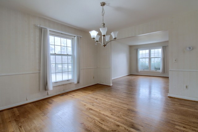 empty room featuring plenty of natural light, a notable chandelier, visible vents, and wood finished floors
