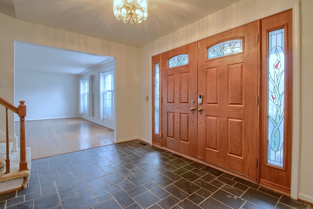 entrance foyer featuring baseboards, an inviting chandelier, stairway, and stone tile flooring