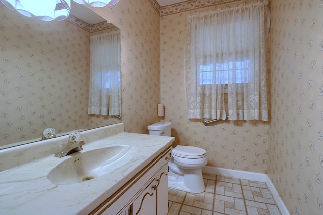 bathroom with baseboards, wallpapered walls, toilet, and vanity